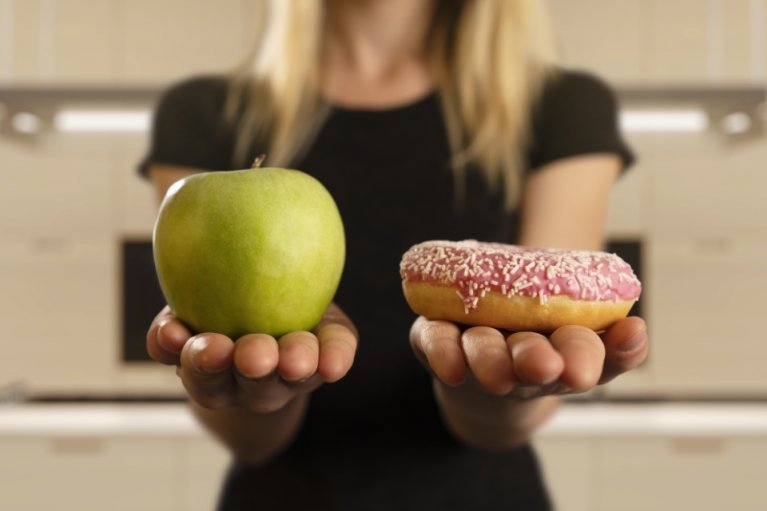 woman holding a green apple in left hand a donut in right hand