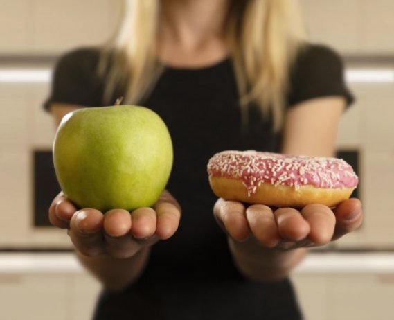 woman holding a green apple in left hand a donut in right hand
