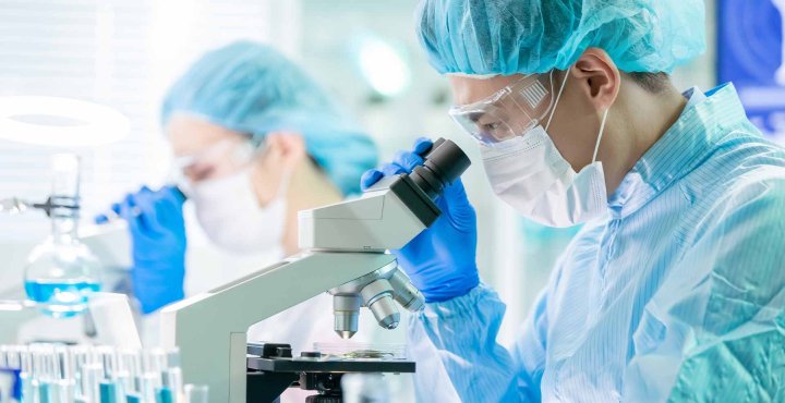 Masked researcher analyzes sample under lab microscope