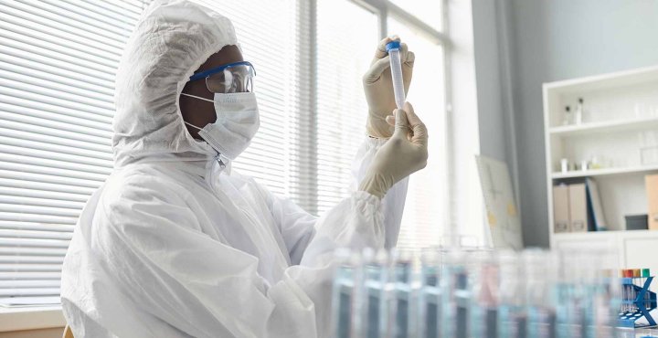 Scientist in lab wearing protective gear examines a sample