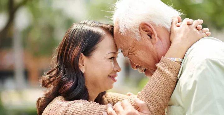 An elderly father presses his forehead against his daughter's in a comforting fashion
