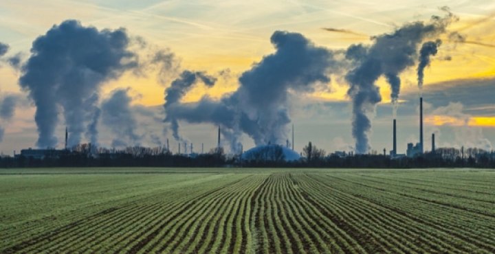 CO2 bi products entering air from smoke stacks next to a field of crops.