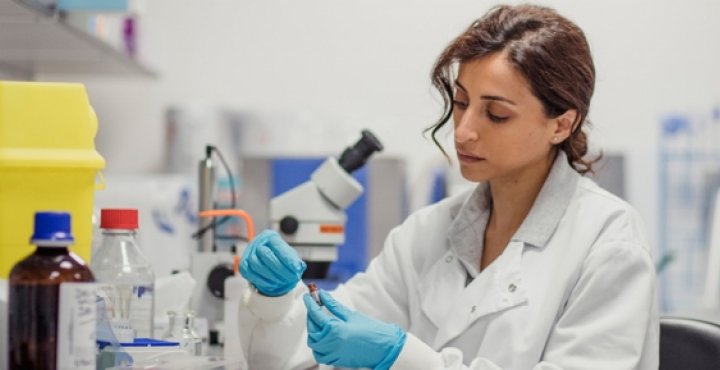 Researcher looks at a slide sample next to a microscope.