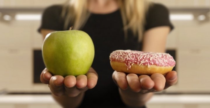 woman holding a green apple in left hand a donut in right hand