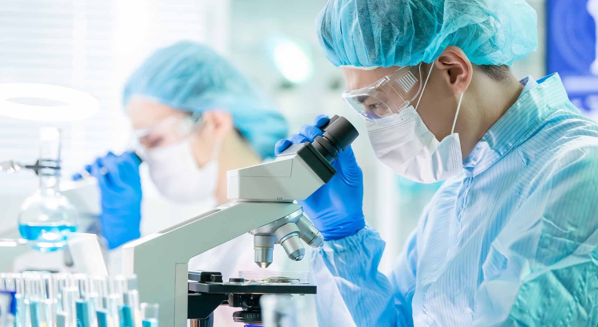 Masked researcher analyzes sample under lab microscope