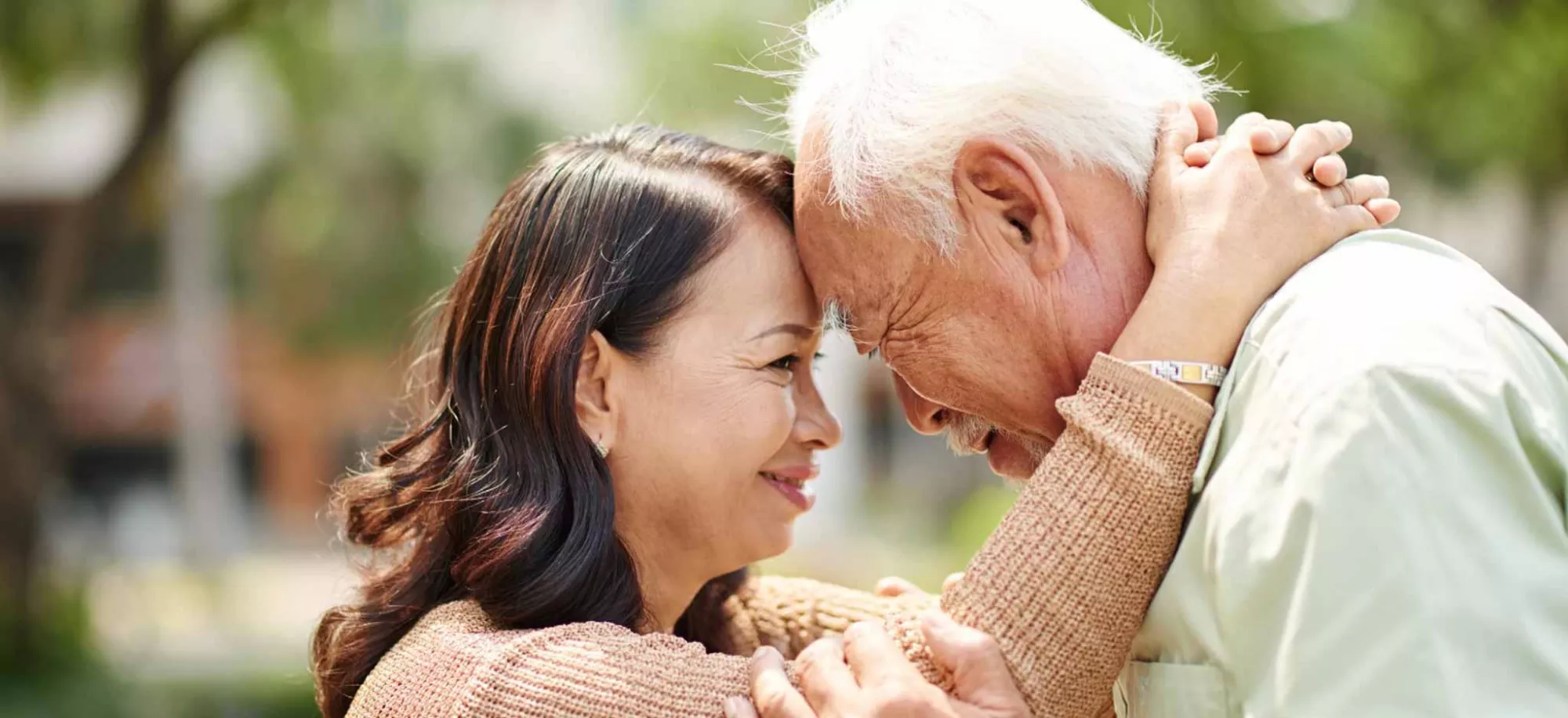 An elderly father presses his forehead against his daughter's in a comforting fashion