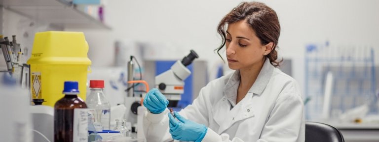 Researcher looks at a slide sample next to a microscope.